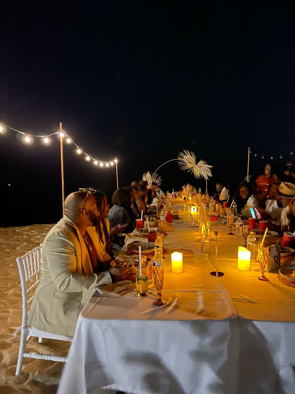 A long dinner table set with candles and string lights on the beach at night in Los Cabos