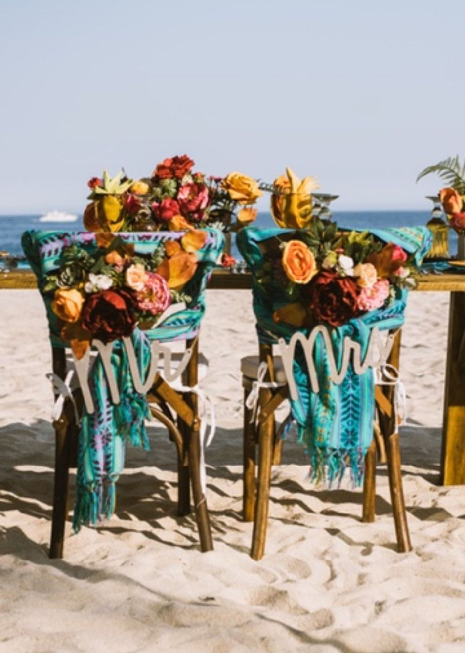Two wooden beach chairs dressed with flowers and Mr and Mrs signs on the sand in Los Cabos