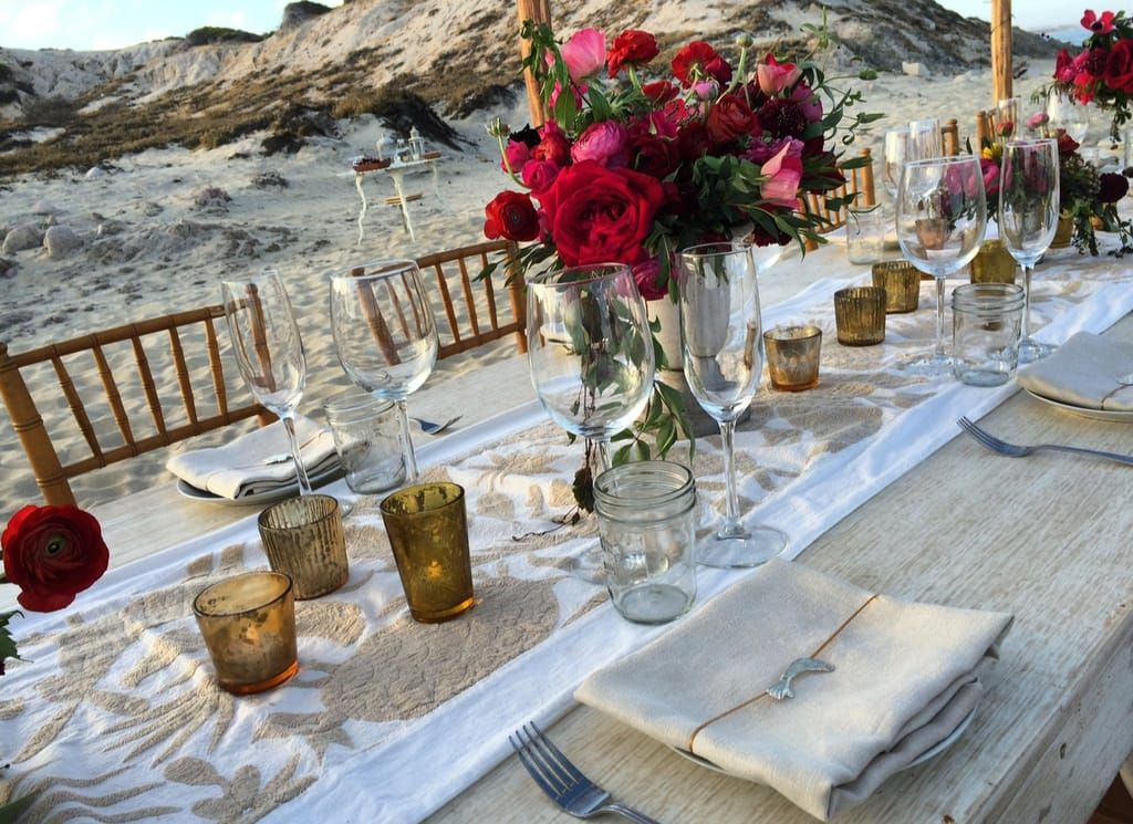A beachfront table setting with red roses, candles and polished glassware