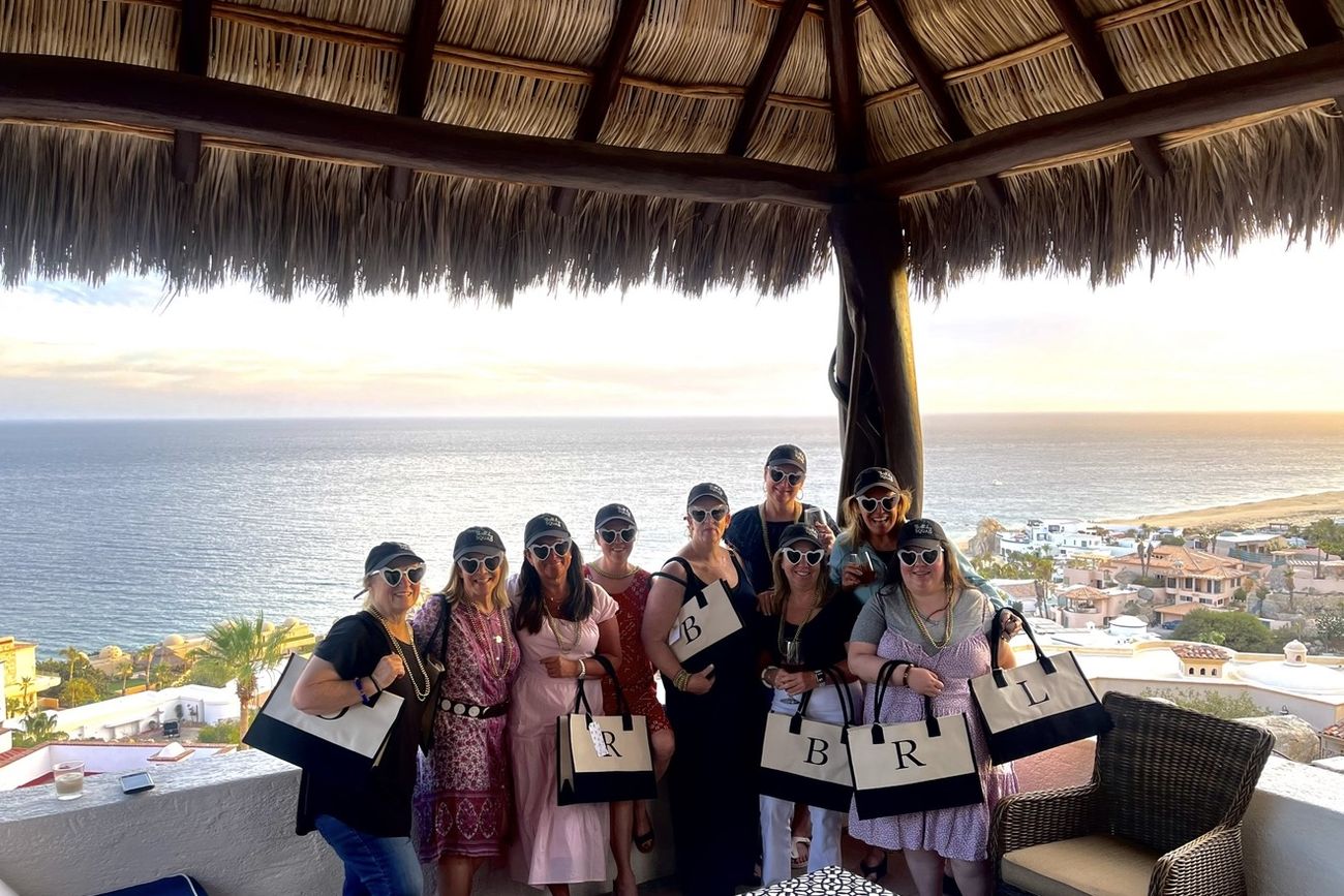 The bride and her friends with personalised tote bags under a palapa at sunset in Los Cabos