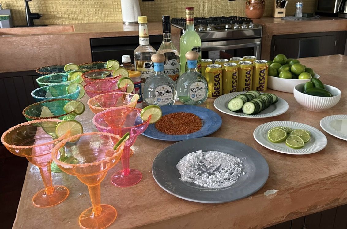 A margarita bar set up on a villa kitchen island with tequila, limes and salted glasses